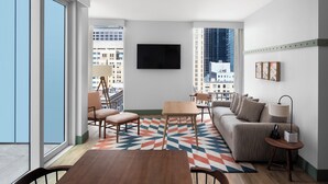 Een moderne woonkamer met een bank, stoelen, een salontafel en een aan de muur bevestigde televisie.