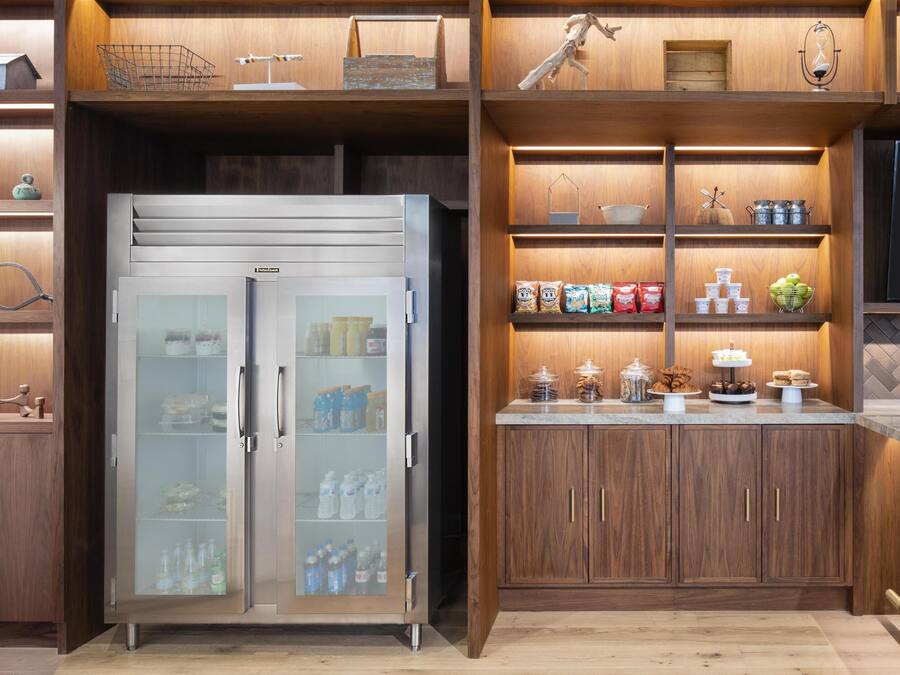 Een moderne keuken met een roestvrijstalen koelkast, houten keukenkastjes en diverse etenswaren op planken.