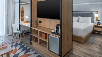 A hotel room with a bed, a desk with a computer, a TV, and a small refrigerator.