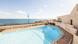 A swimming pool with a view of the sea, a sun lounger area, and a building with a modern design. - Studio Magnifique Vue Mer, Piscine, Climatisation, Terrasse, Parking Couvert (Collioure)