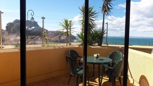 A balcony with a table and chairs, overlooking a coastal view with buildings and a beach. - Studio Magnifique Vue Mer, Piscine, Climatisation, Terrasse, Parking Couvert (Collioure)