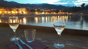 A table with two wine glasses and a water glass, overlooking a body of water with buildings in the background. - Studio Magnifique Vue Mer, Piscine, Climatisation, Terrasse, Parking Couvert (Collioure)
