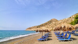 A beach with rows of blue lounge chairs and thatched umbrellas.