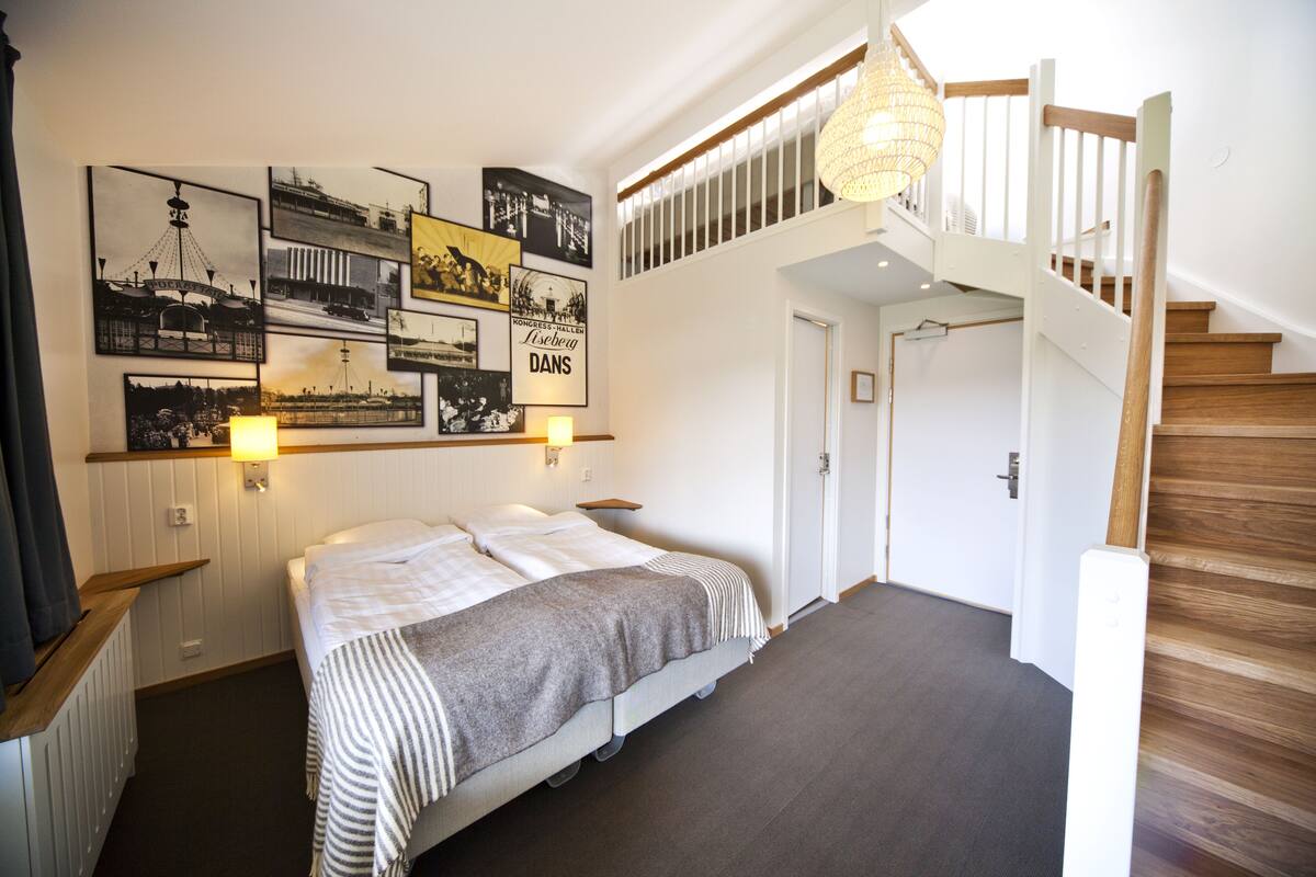 Una camera d'albergo con un letto, una scala e quadri appesi al muro.