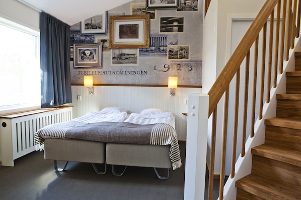 A room with a bed, a wall with framed pictures, a staircase, and a window with curtains. - Lisebergsbyn Bed & Breakfast (Gothenburg)