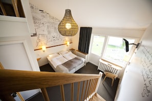Un dormitorio con cama, escritorio, silla, mapa en la pared y ventana con cortinas.