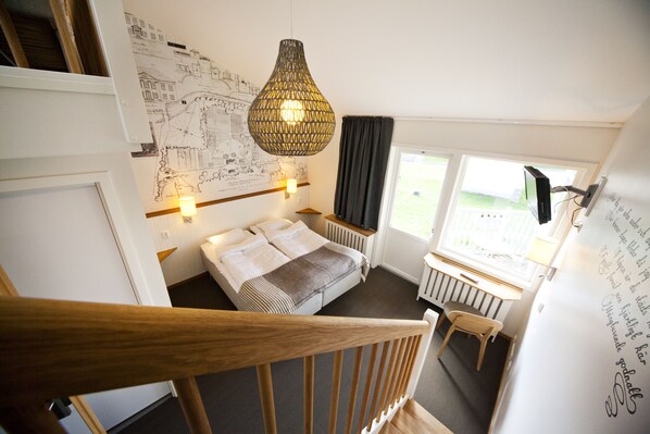 A bedroom with a large bed, a wooden staircase, a map on the wall, and a window with a view of the outdoors.