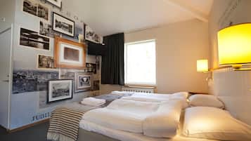 A hotel room with a large bed, a wall decorated with black and white photos, a window with curtains, and a bedside lamp.