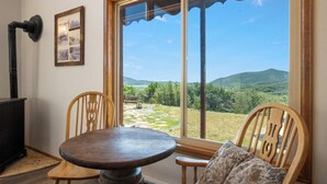Un comedor con mesa y sillas, chimenea y un ventanal con vistas al paisaje.