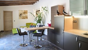 A modern kitchen with a wooden countertop, a built-in oven, and a sink. There is a dining area with a table and chairs, and a green sofa. A large potted plant is in the corner.
