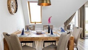 Un coin repas comprenant une table en bois, six chaises, une grande fenêtre et une horloge murale décorative.