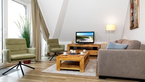 Un salon moderne comprenant un téléviseur, deux fauteuils, un canapé et une table basse.