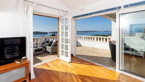 A spacious balcony with a view of the sea, a wooden floor, a TV, and a sofa.