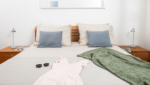 A neatly made bed with pillows, a blanket, and sunglasses on the bed. There are two bedside tables with lamps and a magazine on one of them.