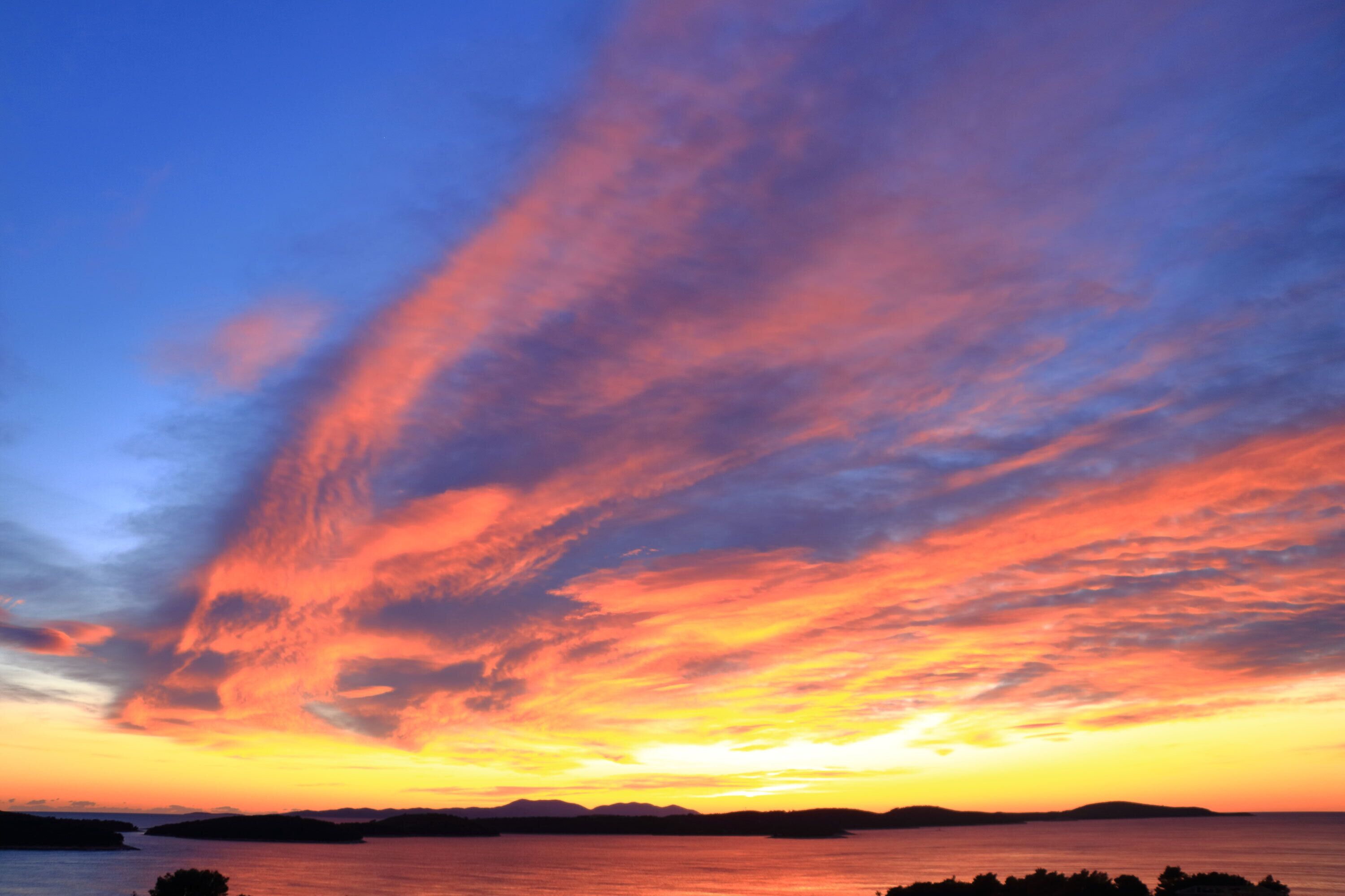 A sunset over a calm body of water with silhouettes of land in the distance.