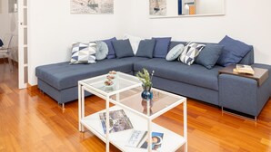 A modern living room with a grey sectional sofa, a glass coffee table, and a wooden floor.