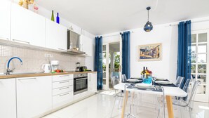 A modern kitchen with white cabinets, a wooden countertop, and a dining area with a white table and clear chairs.