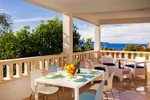 Eine Terrasse mit weißer Möbel, einem Tisch gedeckt mit Tellern und Gläsern, sowie einer Obstschale.