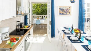 A modern kitchen with white cabinets, a wooden countertop, and a dining area with a white table and blue chairs.