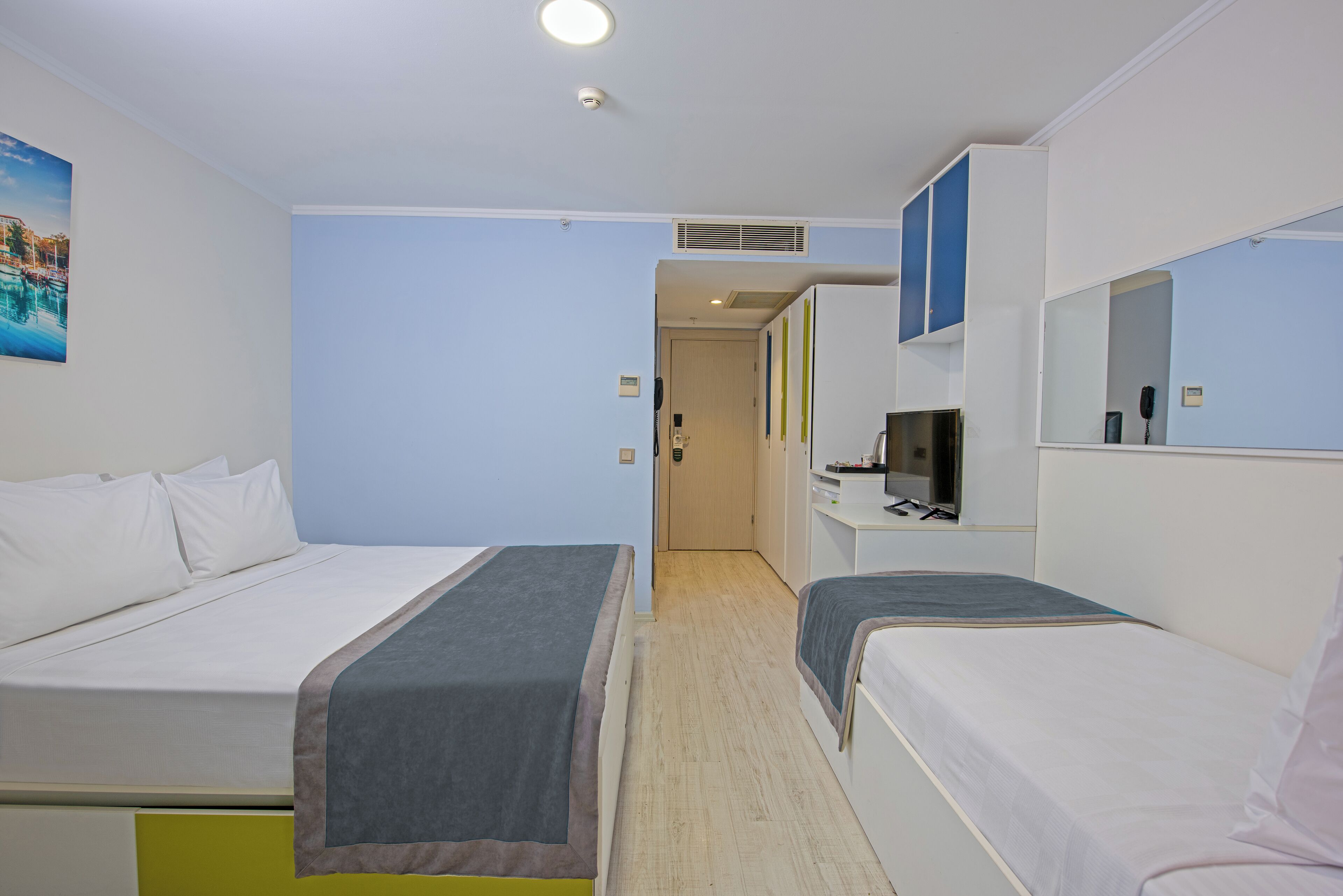 Habitación de hotel con dos camas, un escritorio con computadora, un espejo y un cuadro en la pared.