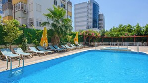 A swimming pool with lounge chairs and umbrellas, surrounded by greenery and buildings. - Citrus Park Hotel (Konyaalti)