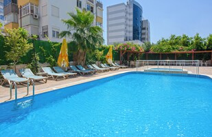 A swimming pool with lounge chairs and umbrellas, surrounded by greenery and buildings.