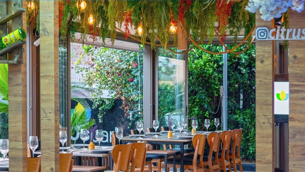 An indoor dining area with wooden tables and chairs, surrounded by glass walls and windows. - Citrus Park Hotel (Konyaalti)