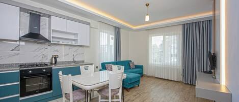 Una cocina moderna con estufa y horno integrados, una mesa de comedor con sillas, un sofá color turquesa y un televisor de pantalla plana montado en la pared.