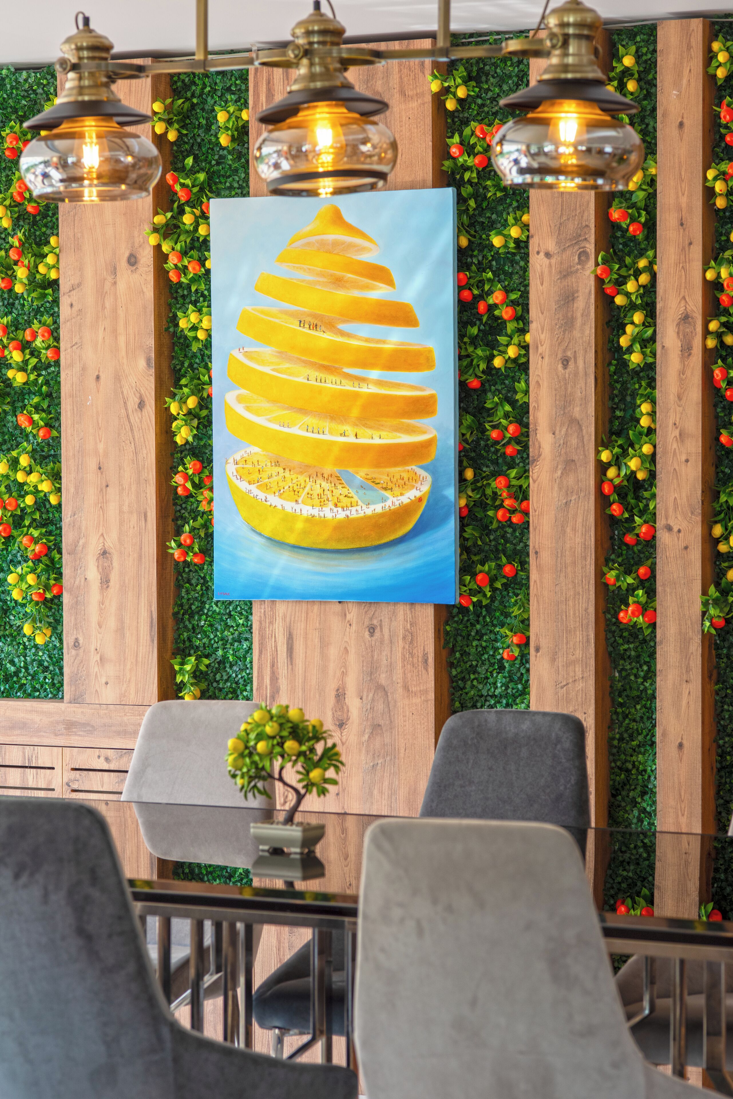 Un espace repas avec des murs lambrissés en bois, une végétation verdoyante et un tableau central représentant un agrume.