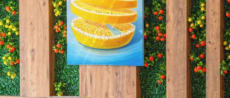 Un espace repas avec des murs lambrissés en bois, une végétation verdoyante et un tableau central représentant un agrume.