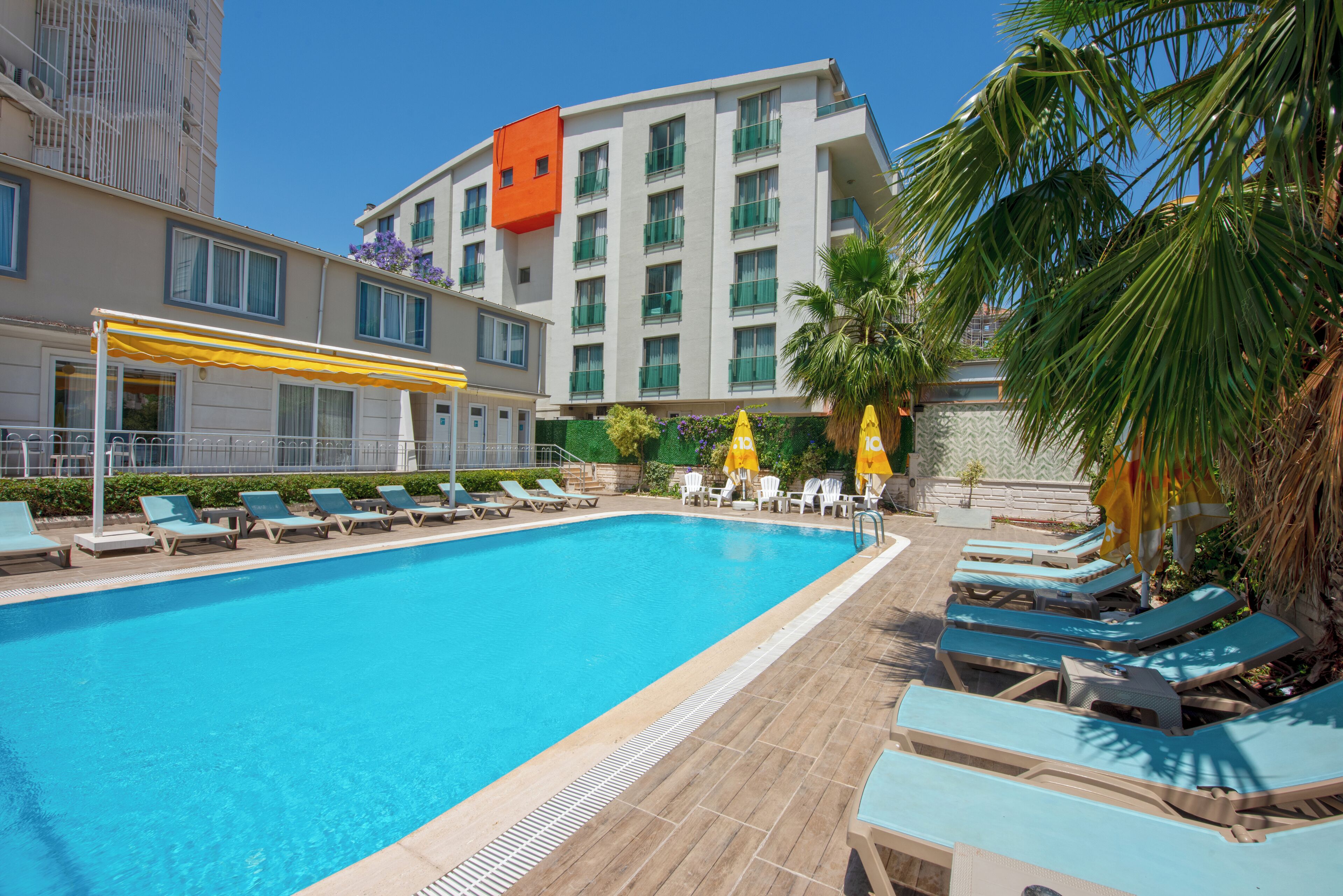 A swimming pool with lounge chairs and umbrellas, surrounded by buildings.