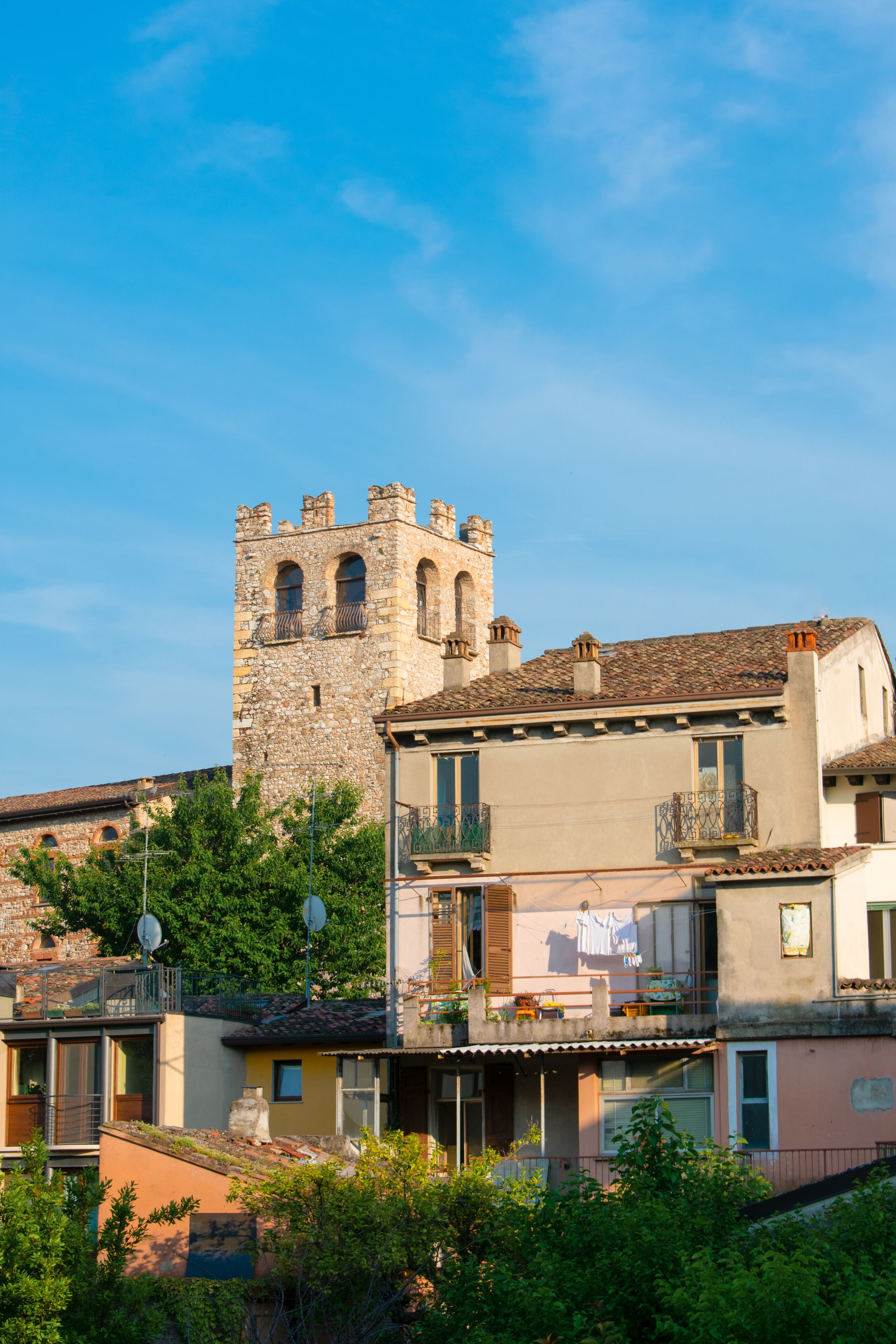 Une tour de pierre historique, dotée d’un balcon, entourée d’immeubles résidentiels également pourvus de balcons et d’antennes paraboliques.