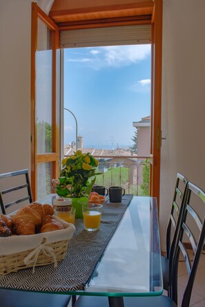 A balcony with a table set for breakfast, including croissants, a vase with flowers, and orange juice glasses.