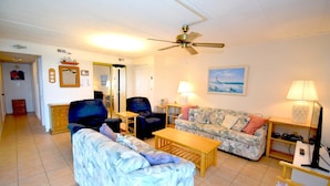 A living room with a sofa, two armchairs, a coffee table, a ceiling fan, and a television. - Thunder Island 80b 2 Bedroom Condo by RedAwning (Ocean City)