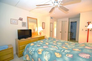 A bedroom with a bed, a TV, a dresser, a mirror, and a ceiling fan. - Thunder Island 80b 2 Bedroom Condo by RedAwning (Ocean City)