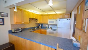 A kitchen with wooden cabinets, a microwave, a stove, and a refrigerator. - Thunder Island 80b 2 Bedroom Condo by RedAwning (Ocean City)