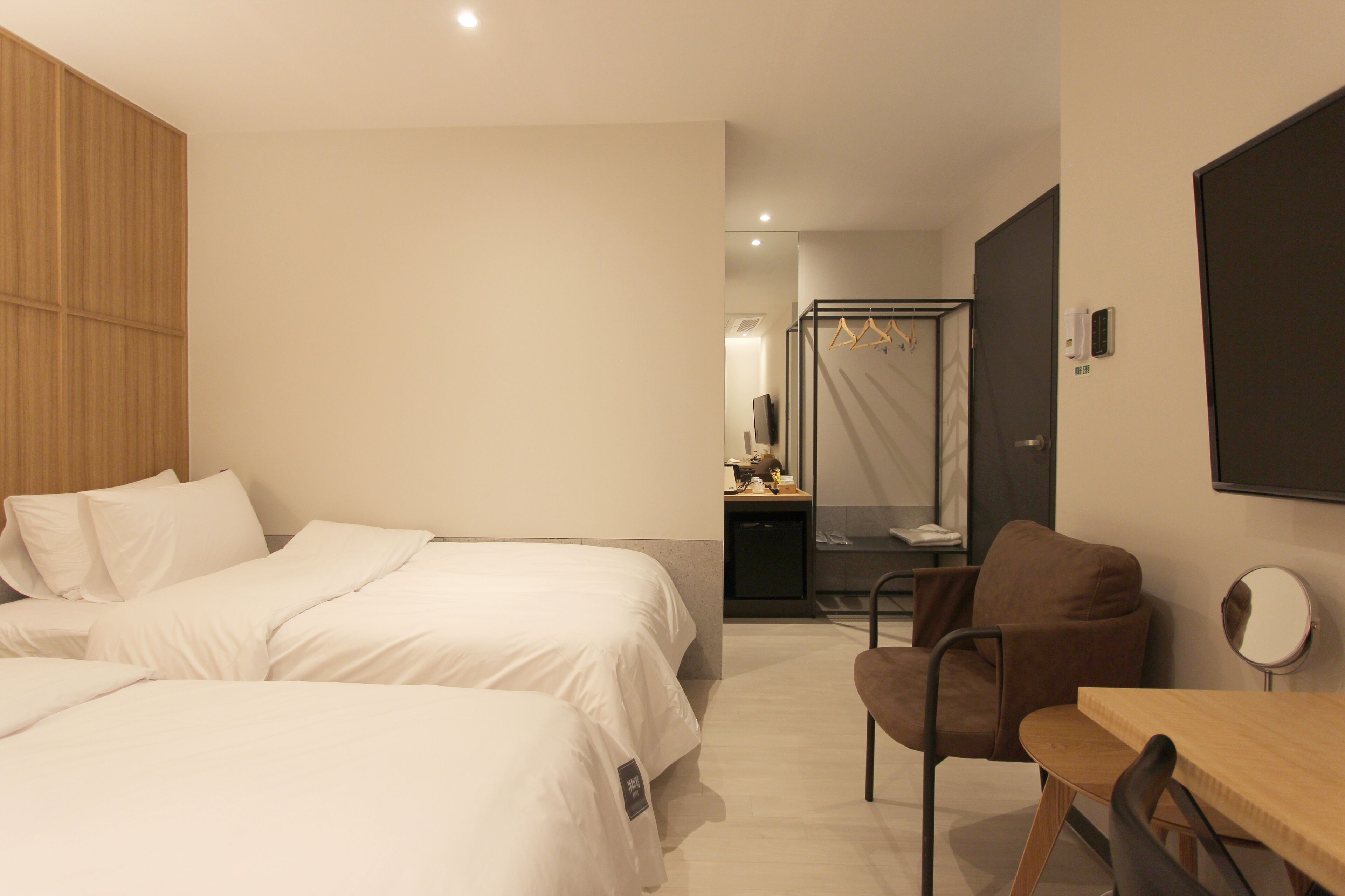 A hotel room with two beds, a wooden wardrobe, a desk with a chair, and a mirror.
