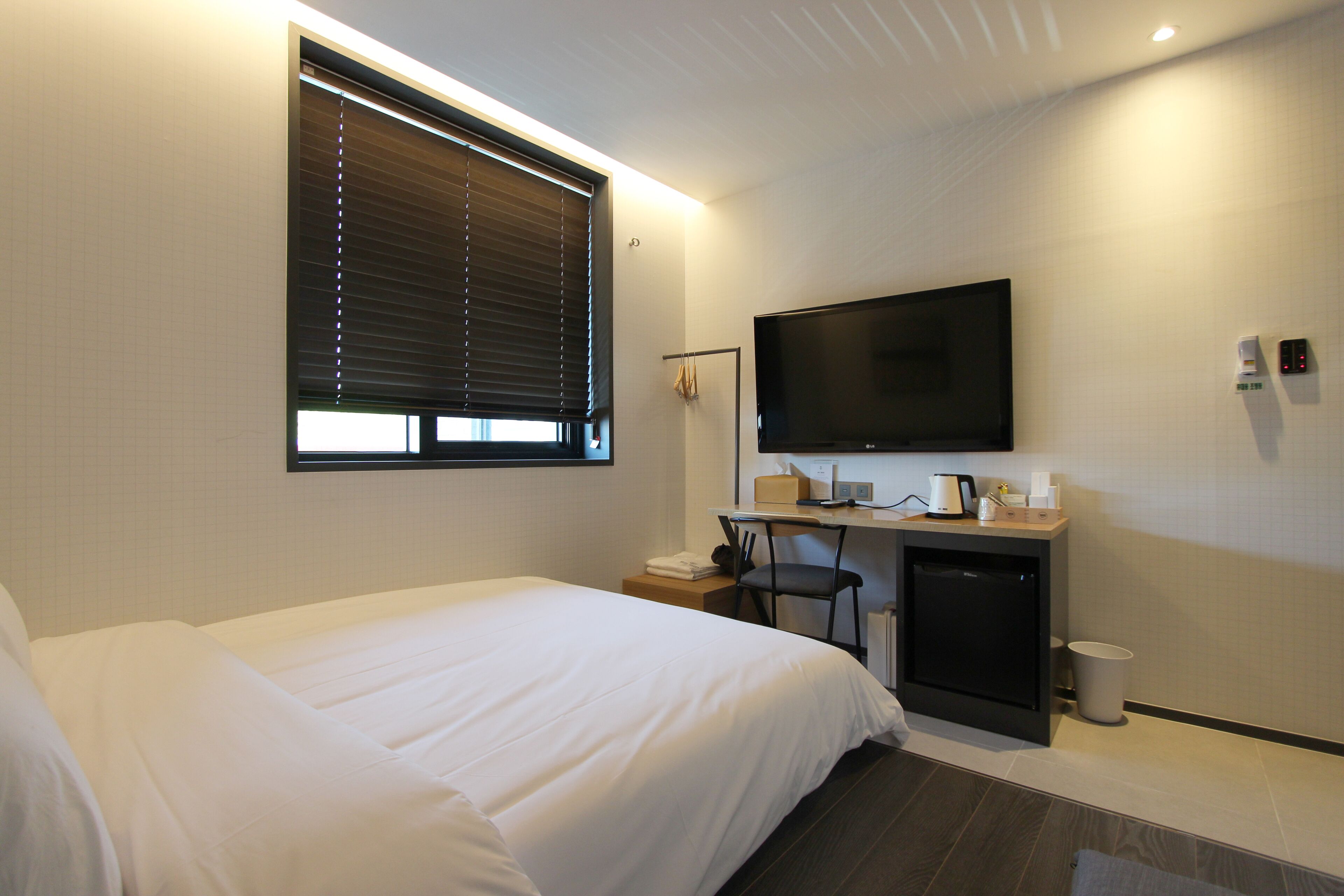 A hotel room with a bed, a desk with a computer, a TV, and a small kitchenette.