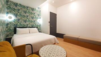 Habitación de hotel moderna con una cama, una mesa redonda, un banco y una pared con estampado tropical.