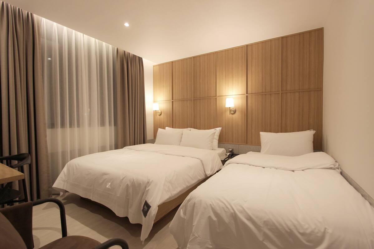 Una habitación de hotel con dos camas, un cabecero de madera y un escritorio con una silla.
