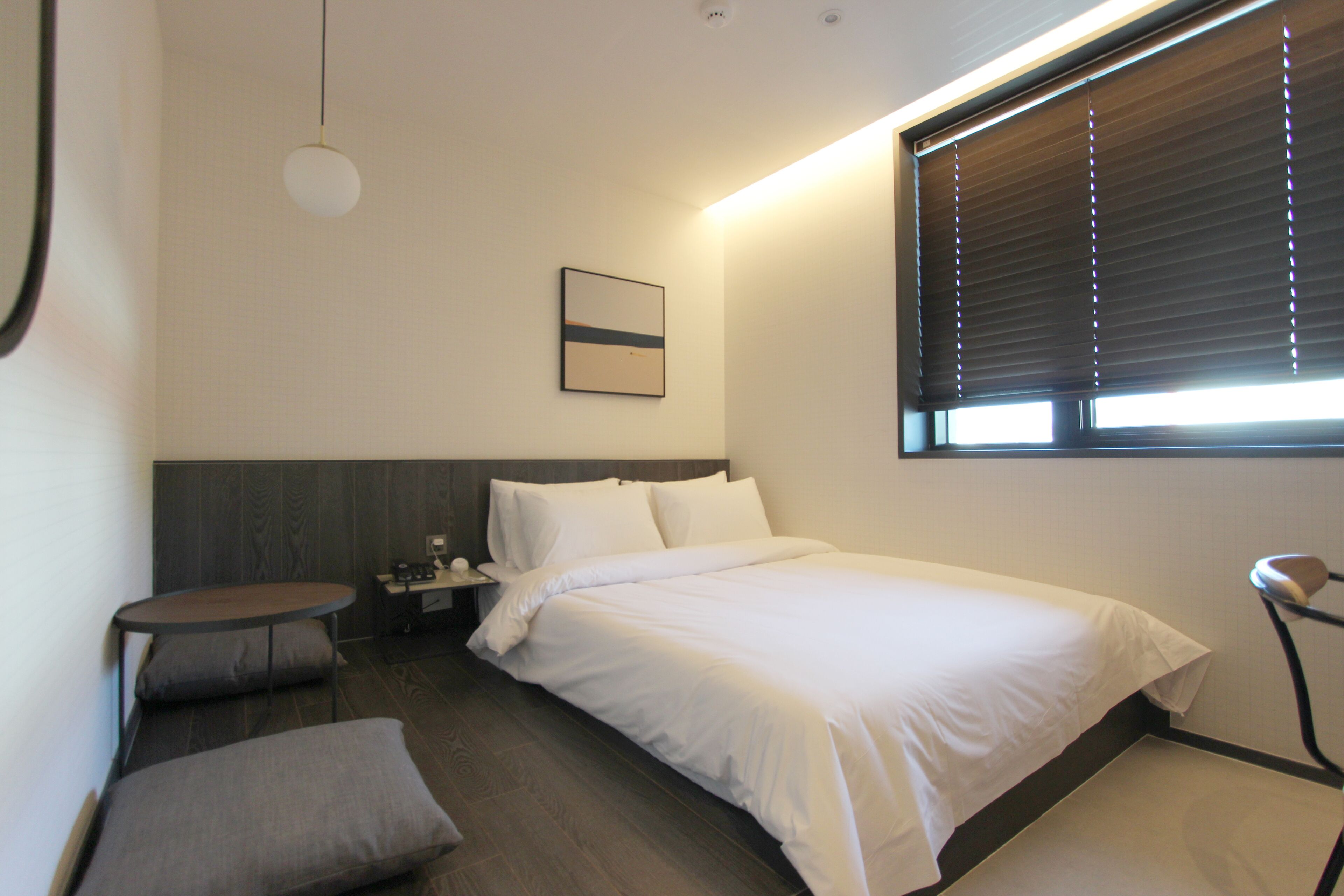 Et moderne hotelværelse med seng, sengebord, lampe og et lille siddeområde.