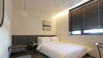 Et moderne hotelværelse med seng, sengebord, lampe og et lille siddeområde.