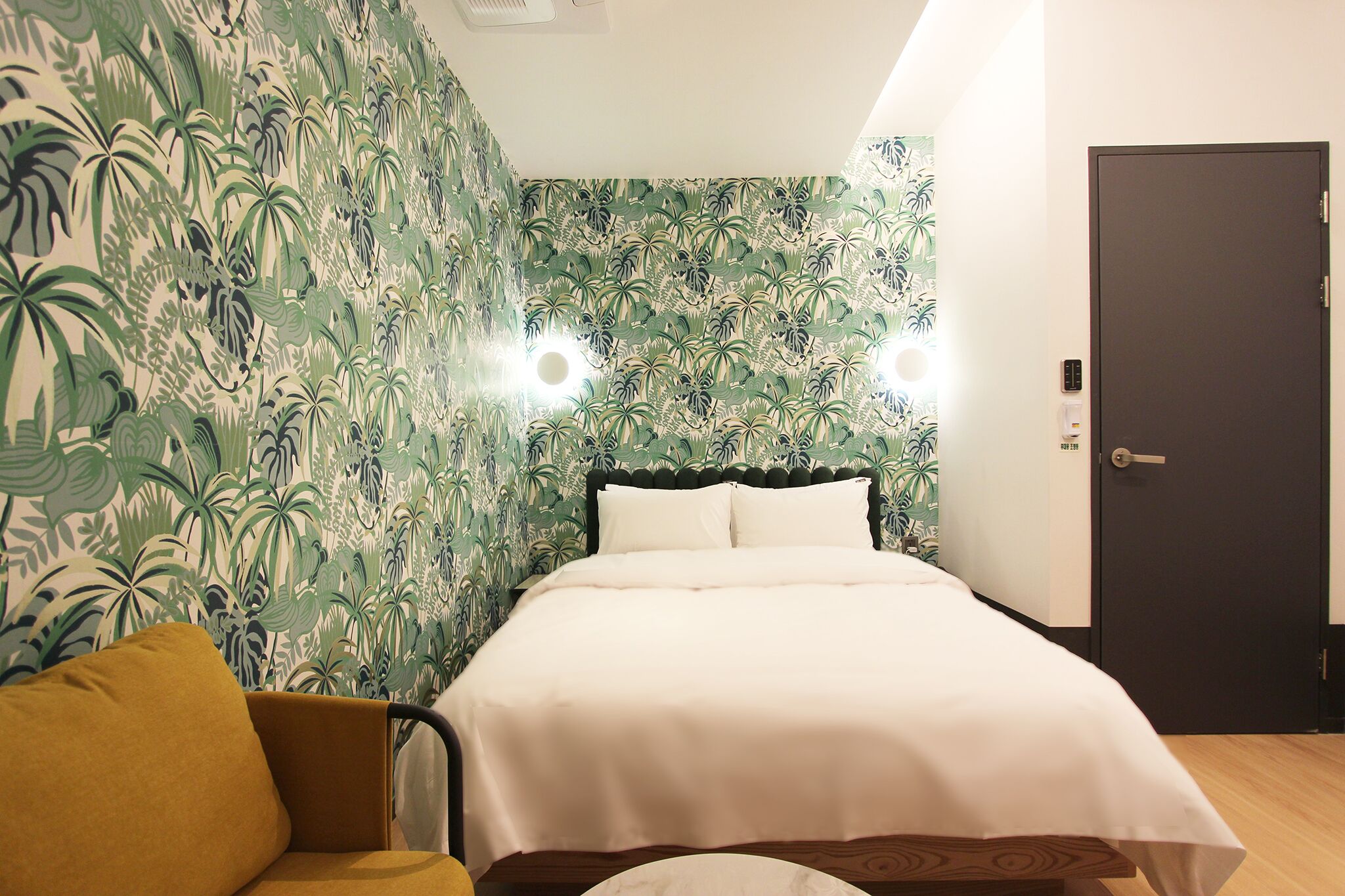 Een slaapkamer met een bed, nachtkastje, stoel en een deur.