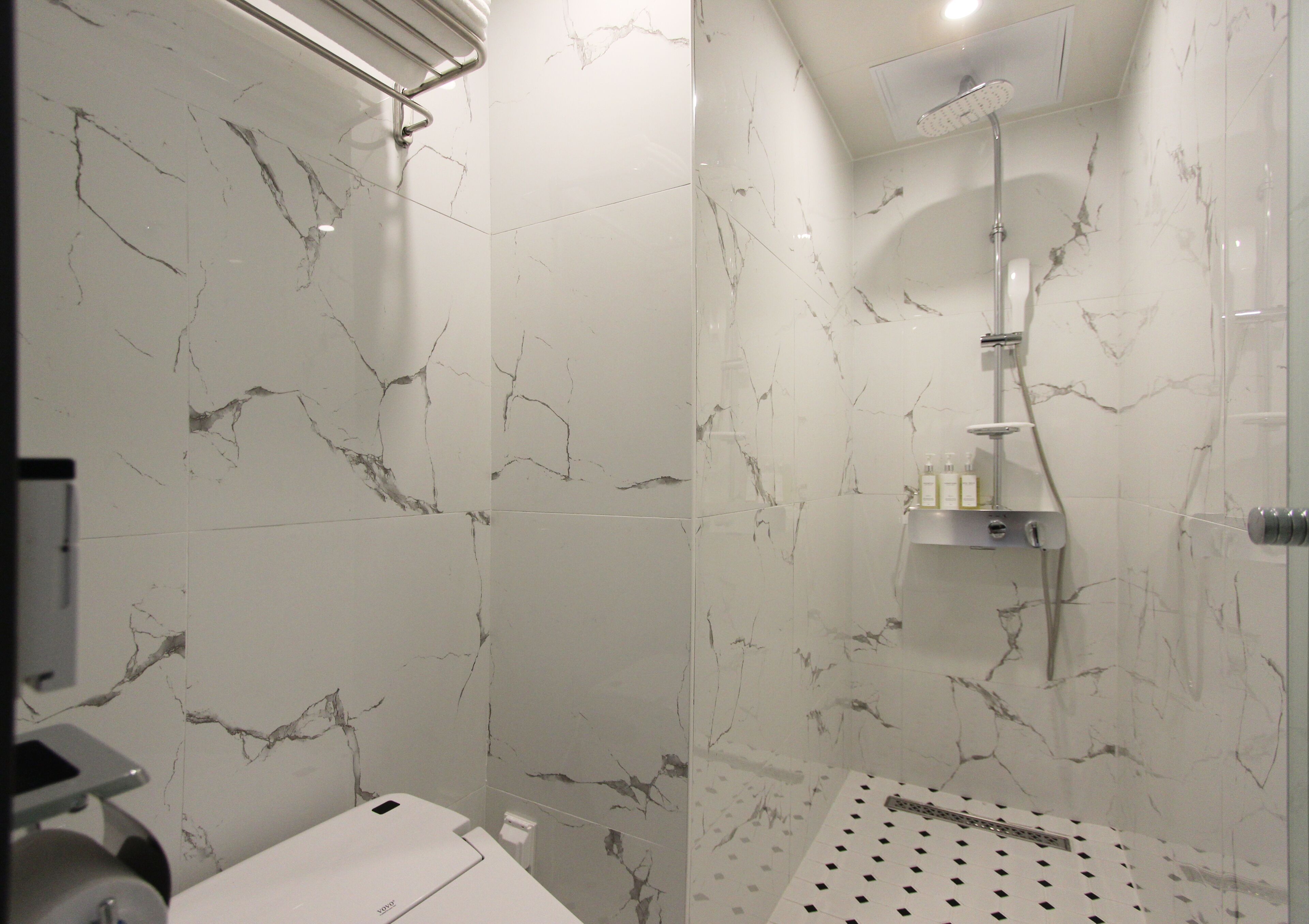 A modern bathroom with marble walls and a shower area.