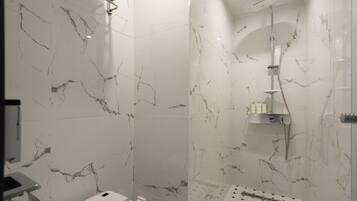 A modern bathroom with marble walls and a shower area.