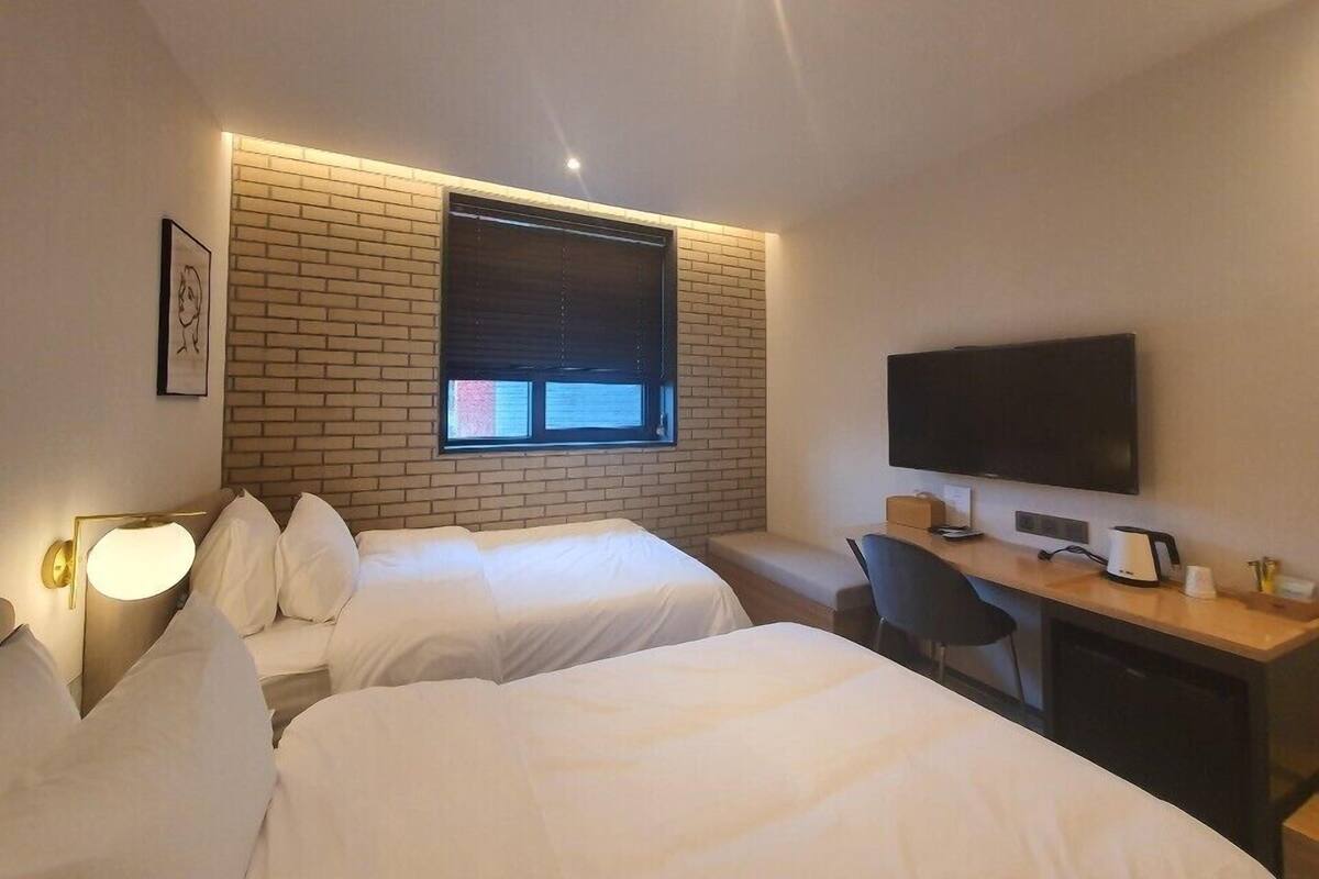 Habitación de hotel con dos camas, un escritorio con ordenador, televisión y ventana con persianas.