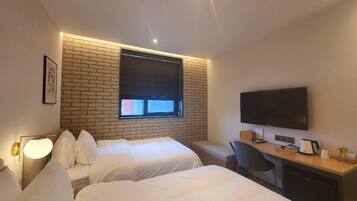 A hotel room with two beds, a desk with a computer, a TV, and a window with blinds.