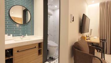 A modern bathroom with a mirror, sink, and toilet. There is a shower area visible through a doorway.