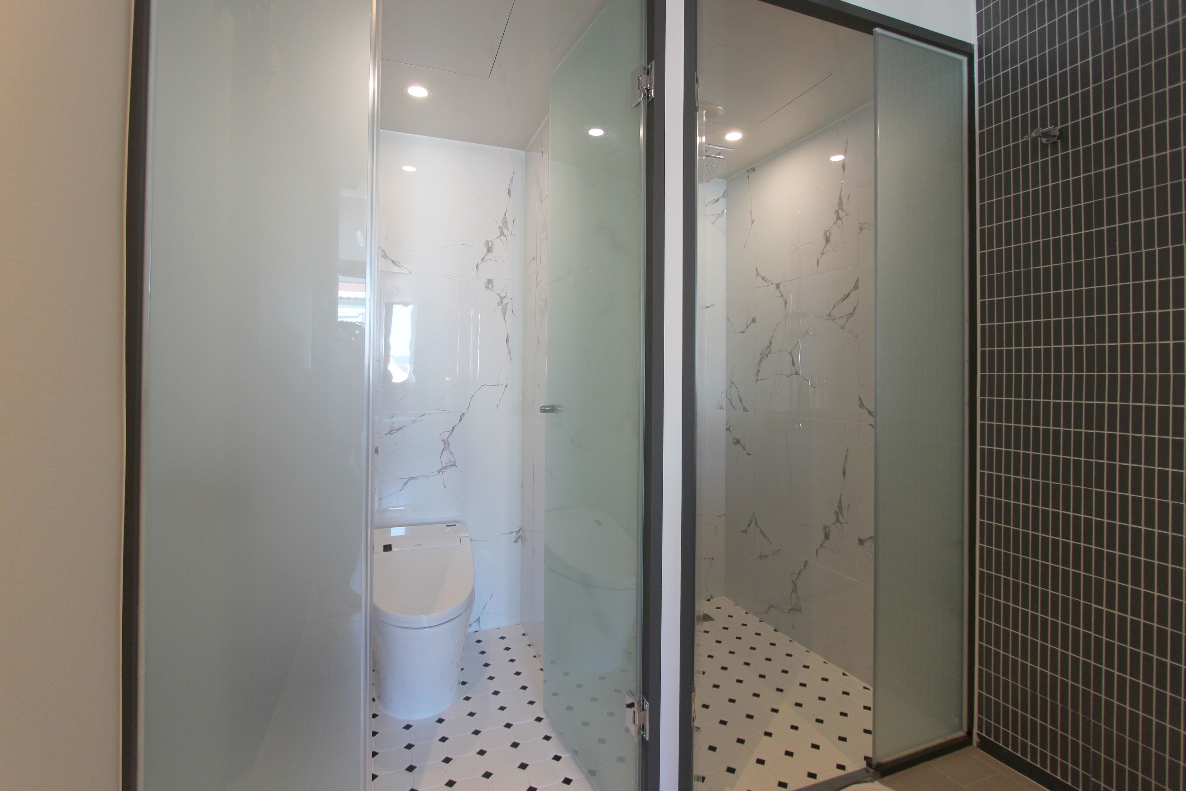 A modern bathroom with a glass shower enclosure, a toilet, and a tiled floor.