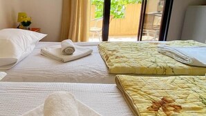 Quarto de hotel com duas camas, cada uma com toalhas dobradas, uma janela com vista para o verde e uma cortina entreaberta.